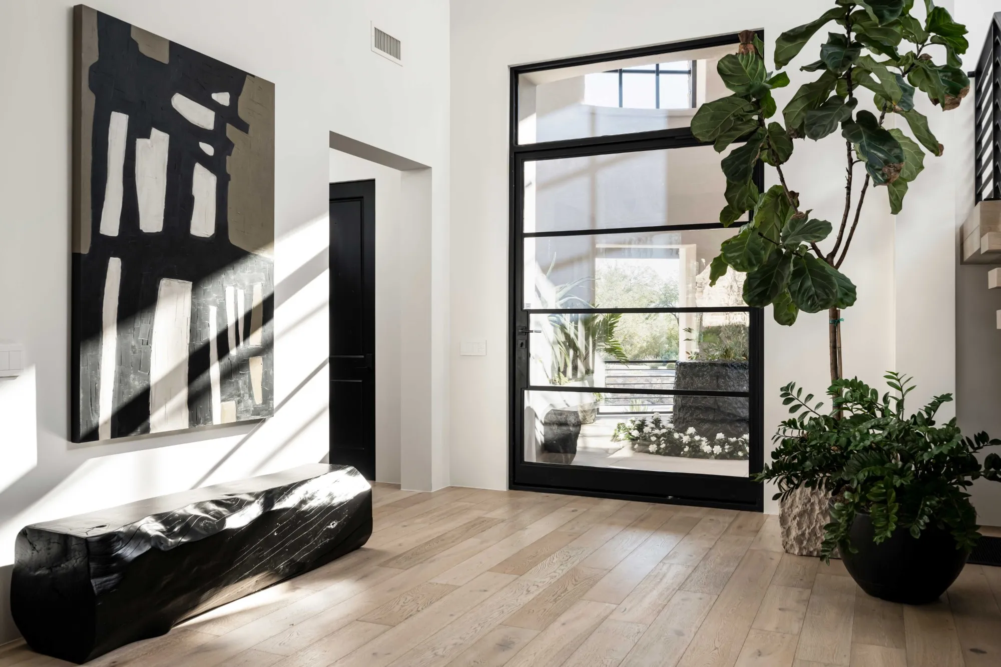 Entryway with abstract art, a fiddle-leaf fig and a black steel-framed door